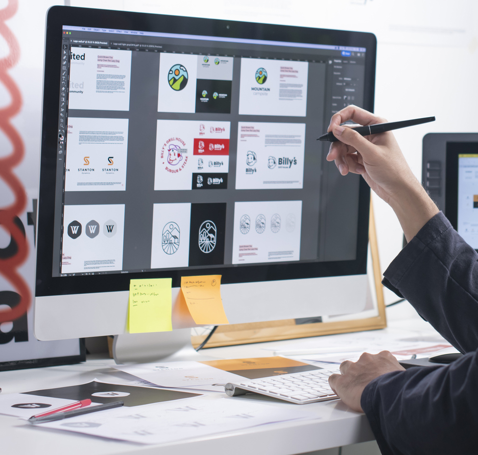 A hand holding a design stylus infront of a computer screen